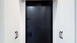 A modern, dark-colored door with a handle and a lock, flanked by white walls and a light-colored floor. - Triphome Nakano 2025 New 6min JR 4min Shinjuku (Nakano City)