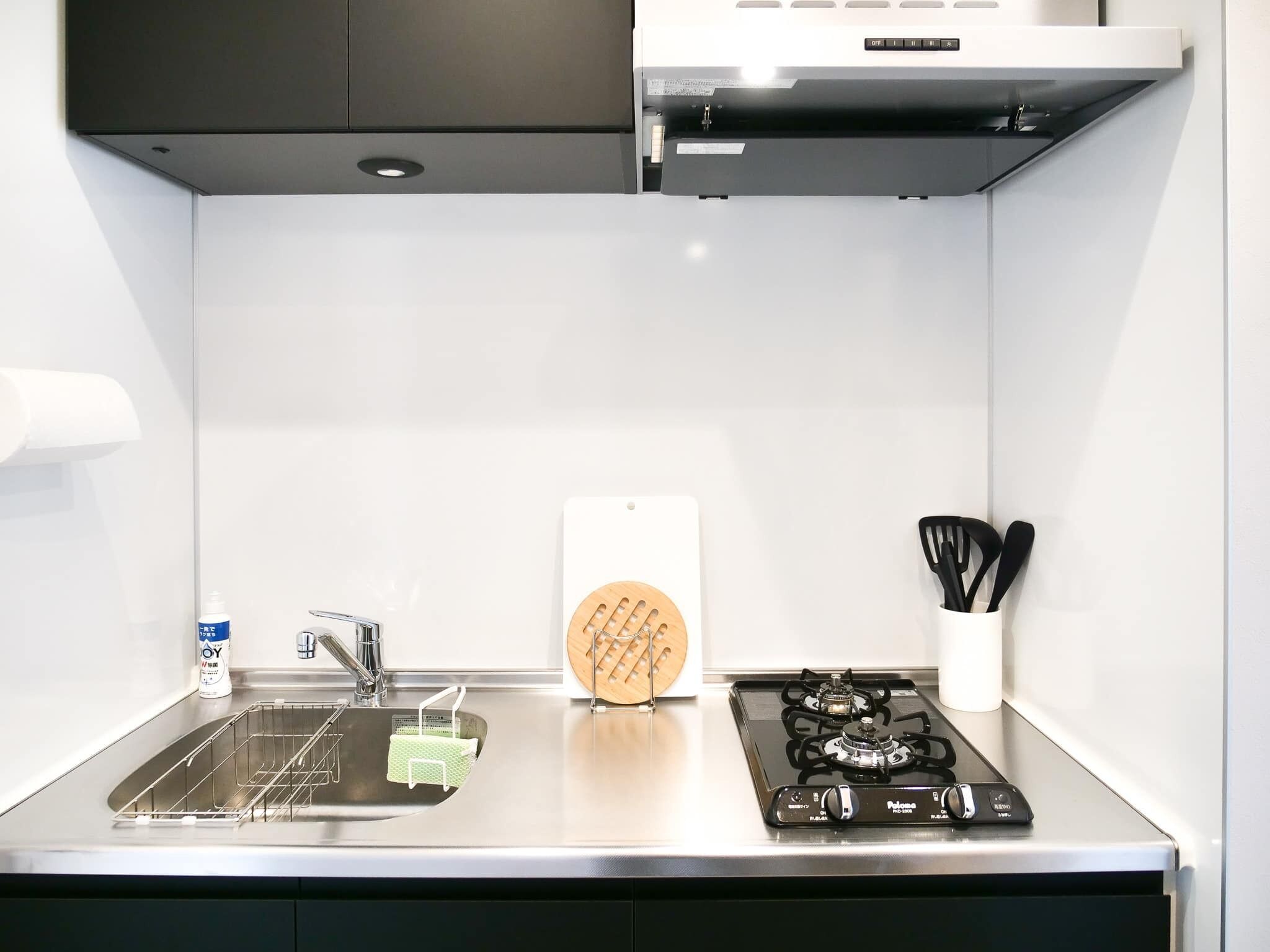 Une cuisine moderne avec un évier en acier inoxydable, une cuisinière à gaz et un mur blanc.