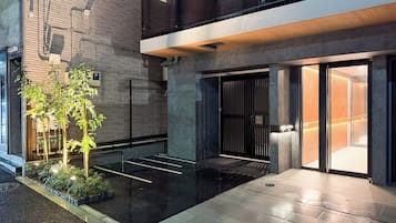 A modern building with a brick facade, a gated entrance, and a small outdoor area with plants.