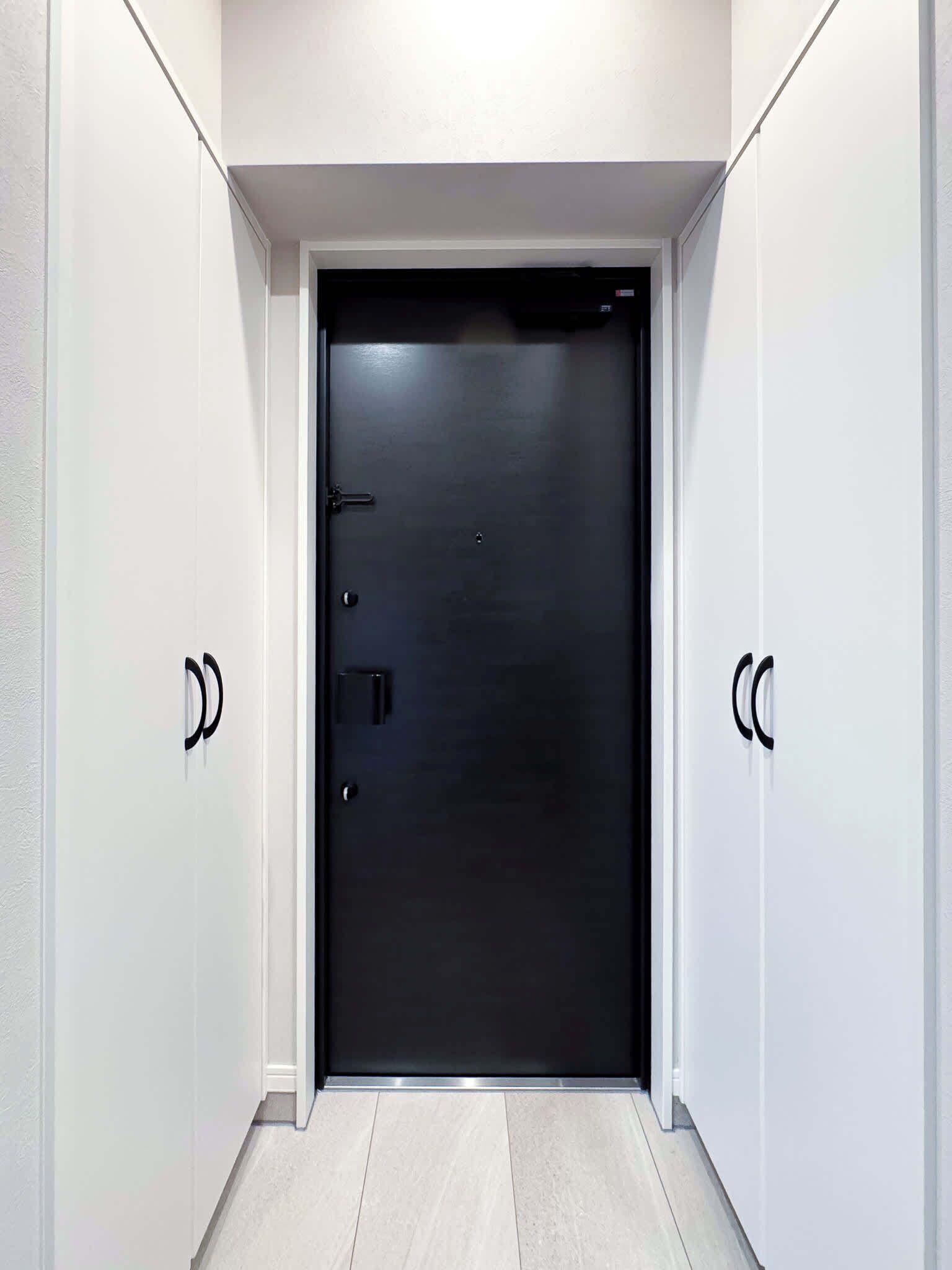 A modern, dark-colored door with a handle and a lock, flanked by white walls and a light-colored floor.