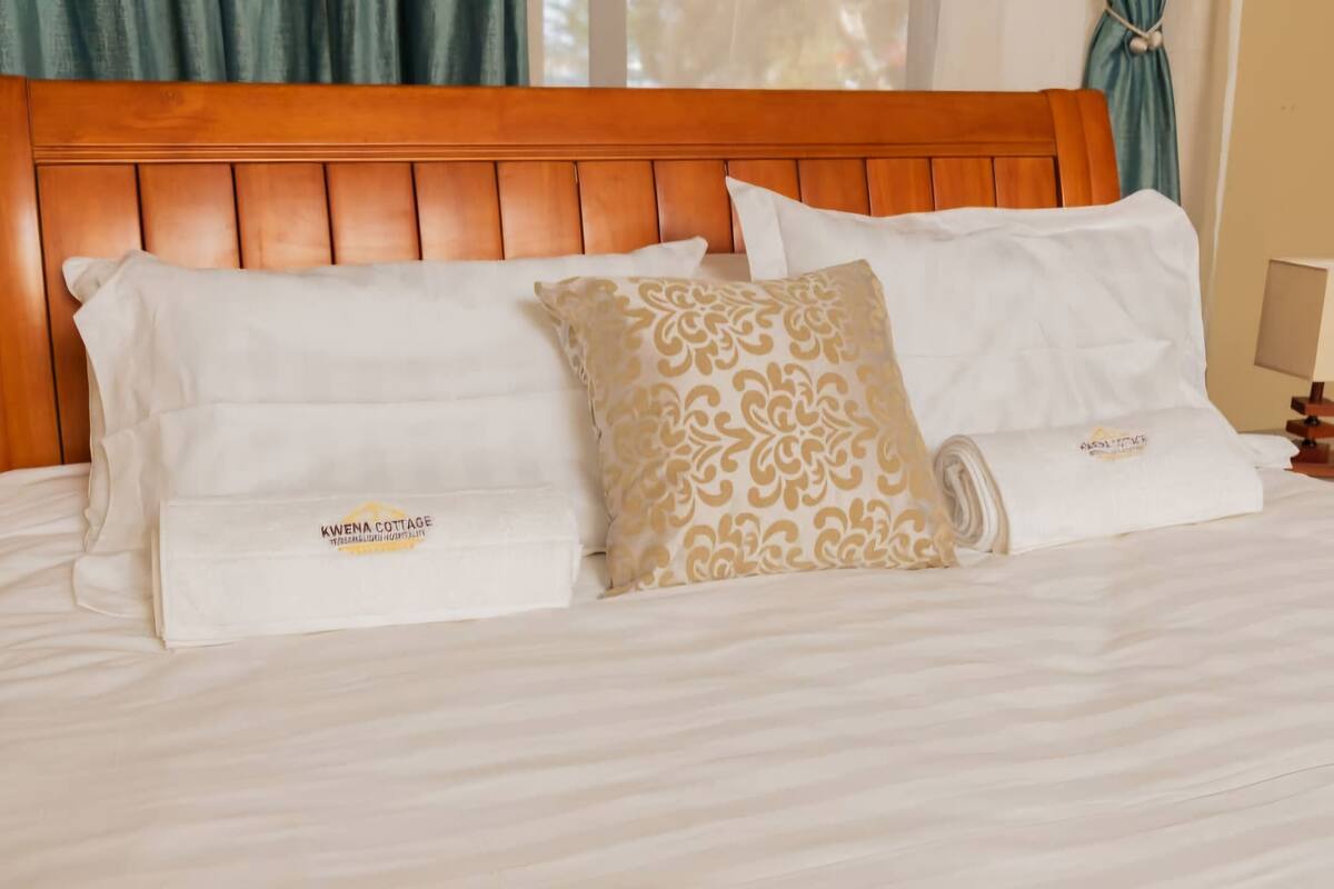 A neatly made bed with white and patterned pillows, a wooden headboard, and a small bedside table with a lamp.