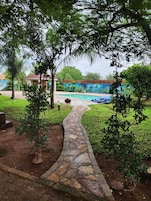 Un camino de piedra que lleva a una piscina rodeada de exuberante vegetación y una pared con murales.