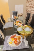 Un comedor con una mesa de vidrio, sillas negras y una variedad de alimentos para el desayuno, como huevos, tocino y tostadas.