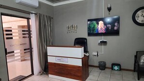 A reception area with a wooden desk, a television mounted on the wall, a clock, and a trash bin.
