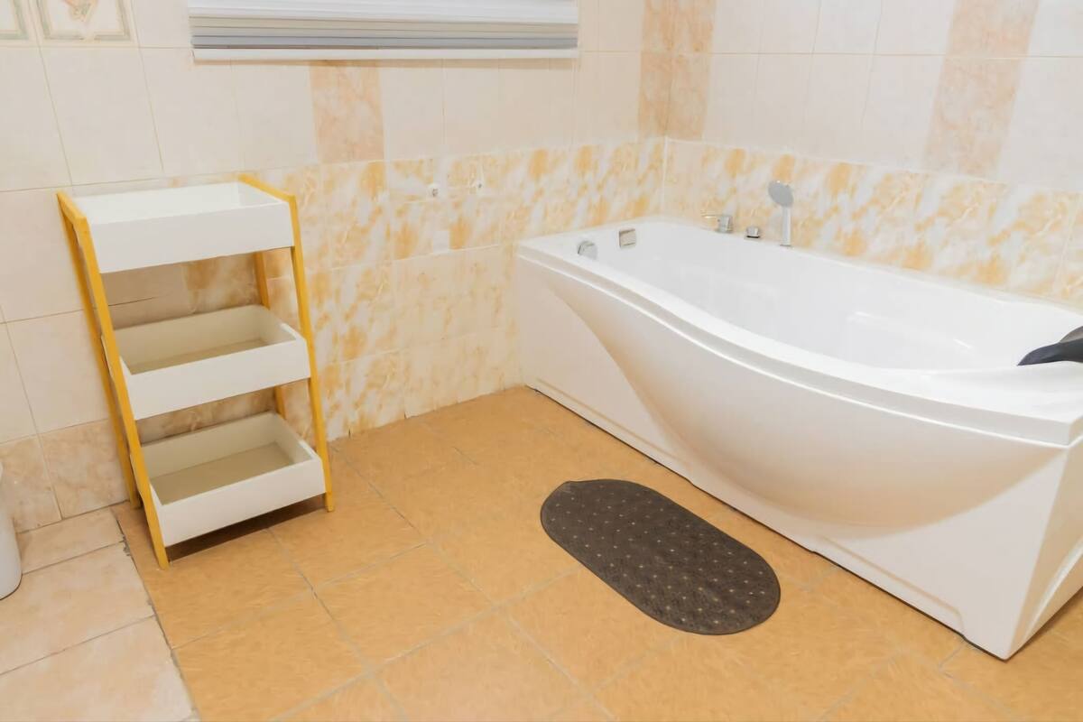 A bathroom with a white bathtub, a yellow shelf unit, and a black mat on the floor.