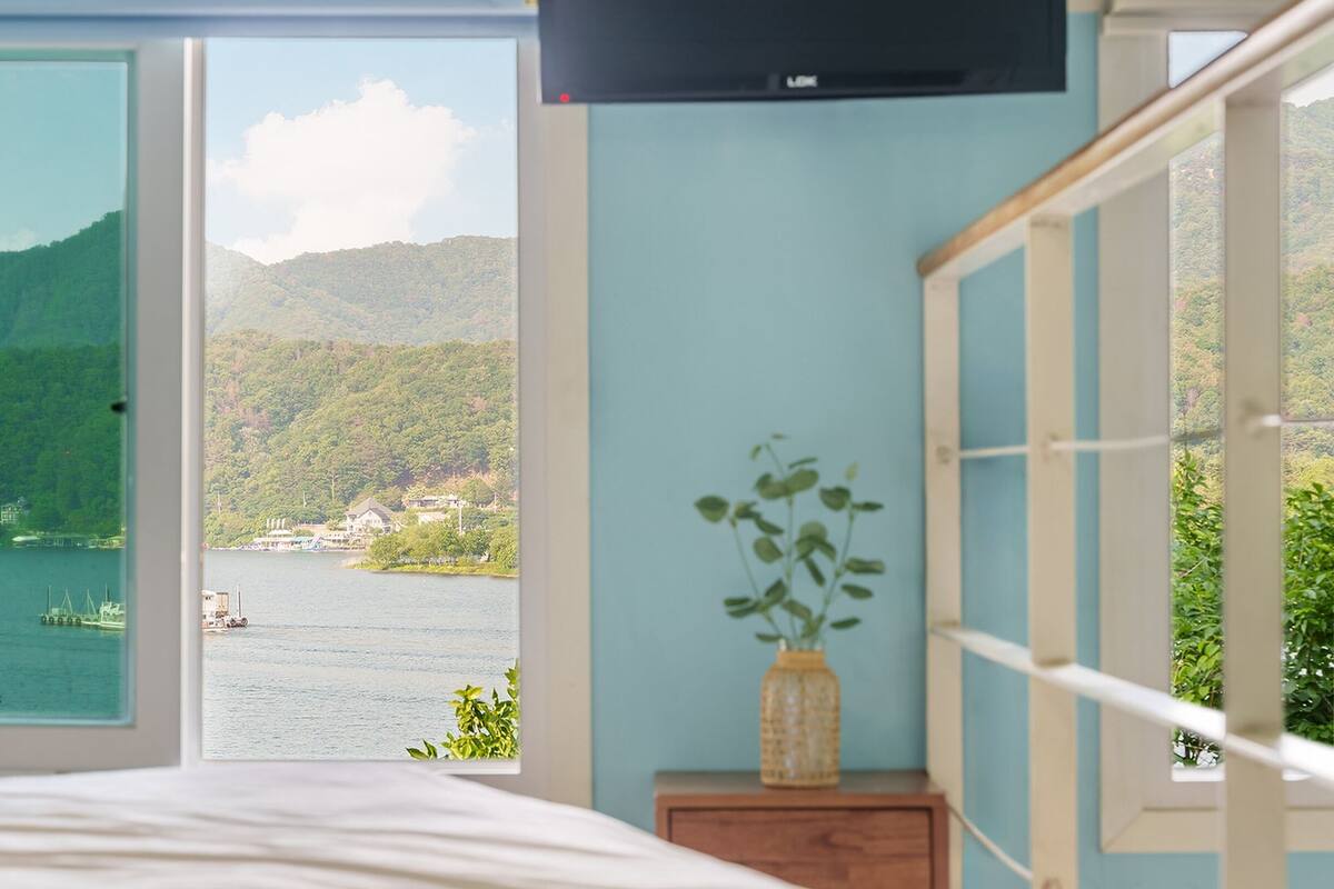 A bedroom with a large window offering a view of a lake and mountains.