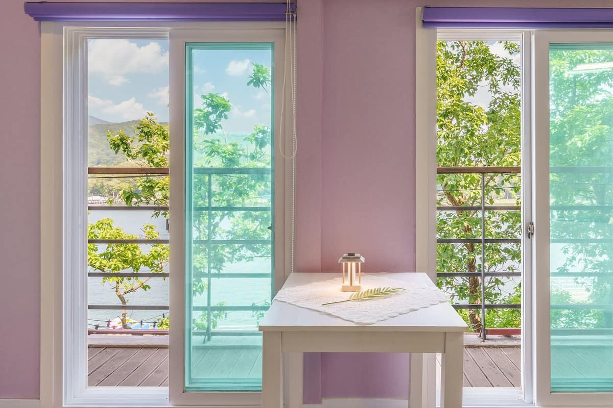 A room with a sliding glass door leading to a balcony with a view of greenery and a body of water.