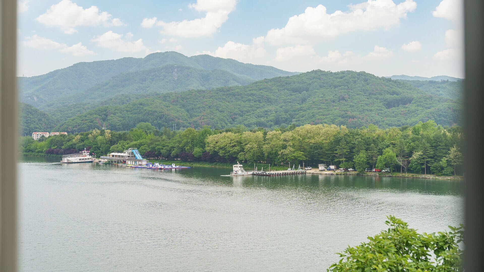 Ein Fluss mit Booten, eine Anlegestelle und ein bewaldeter Berg im Hintergrund.