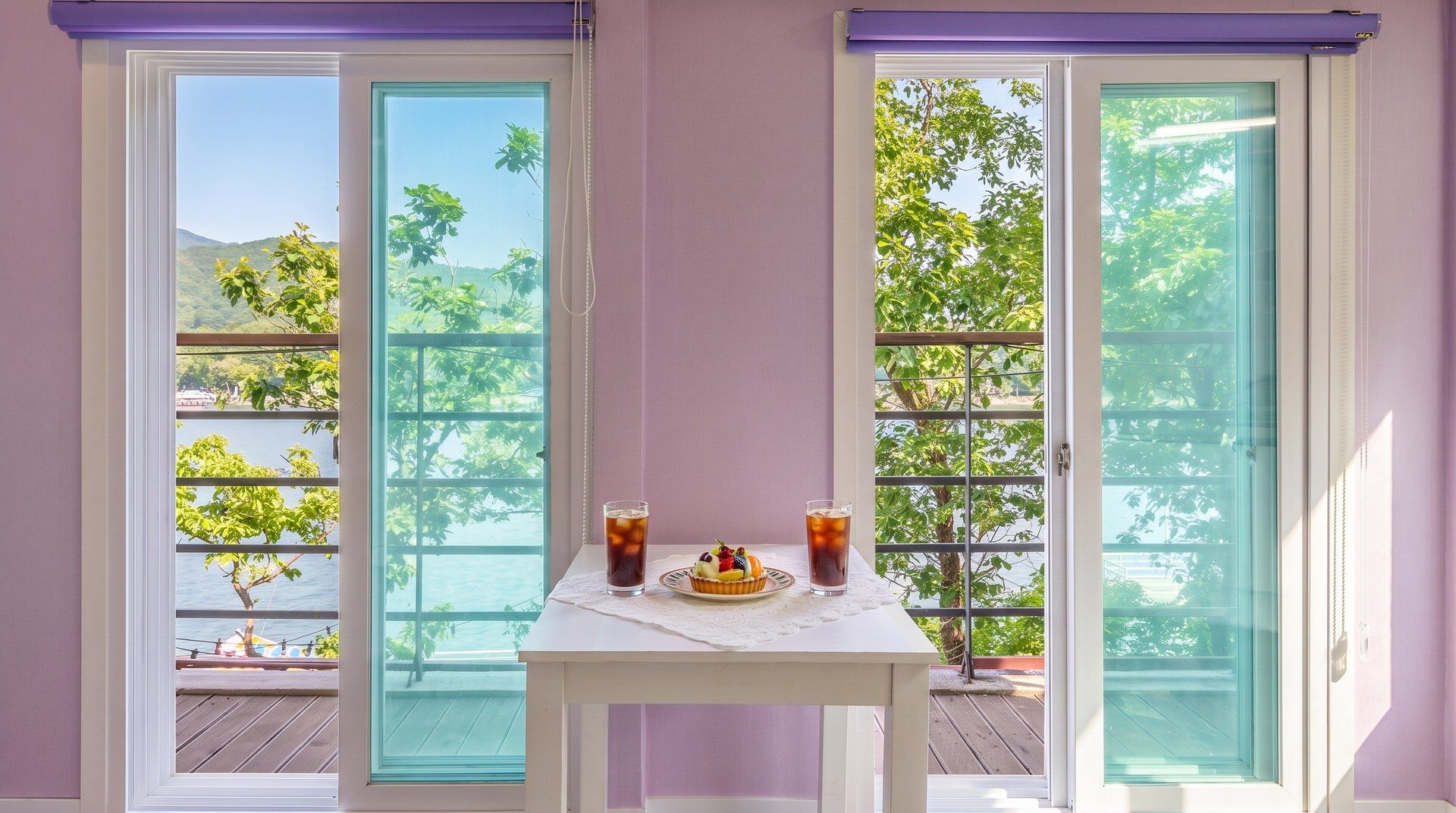 Une table avec un dessert et deux boissons sur un balcon doté de portes vitrées, offrant une vue sur les arbres et l’eau.