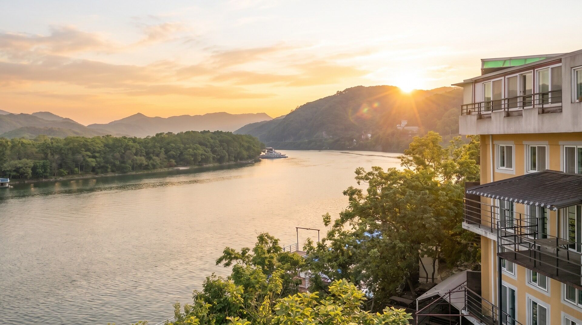 A river with a boat, surrounded by mountains and trees, with a building in the foreground.