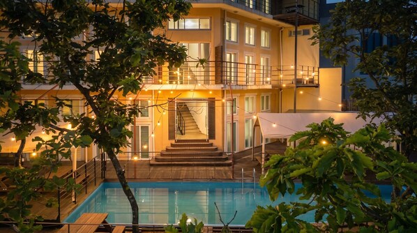 Un edificio de dos pisos con piscina, rodeado de árboles y luces colgantes.