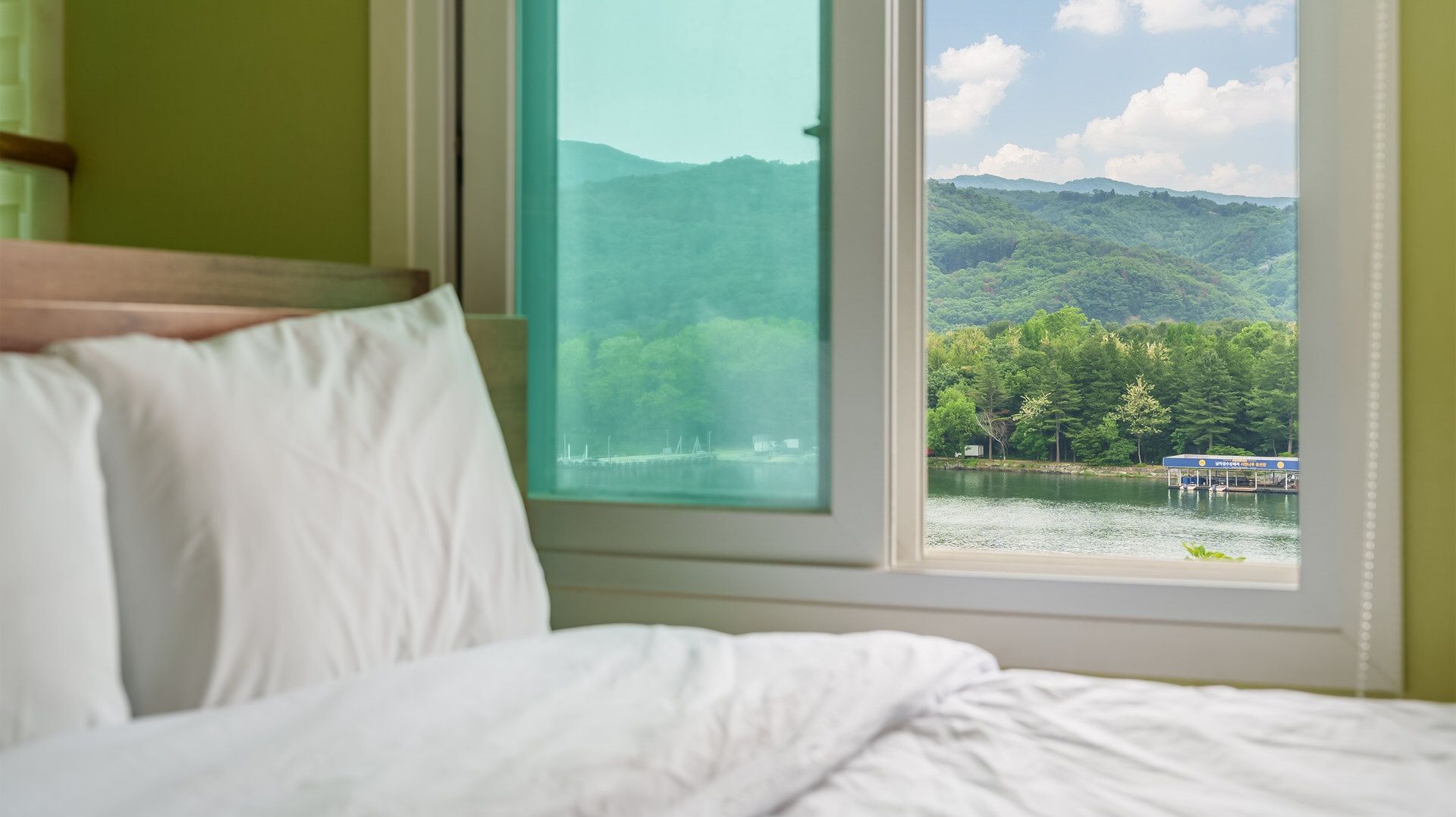 Ein Bett mit weißer Bettwäsche und ein Fenster mit Blick auf einen See und einen Wald.