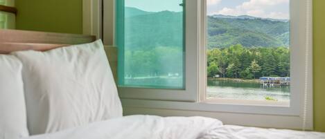 Ein Bett mit weißer Bettwäsche und ein Fenster mit Blick auf einen See und einen Wald.