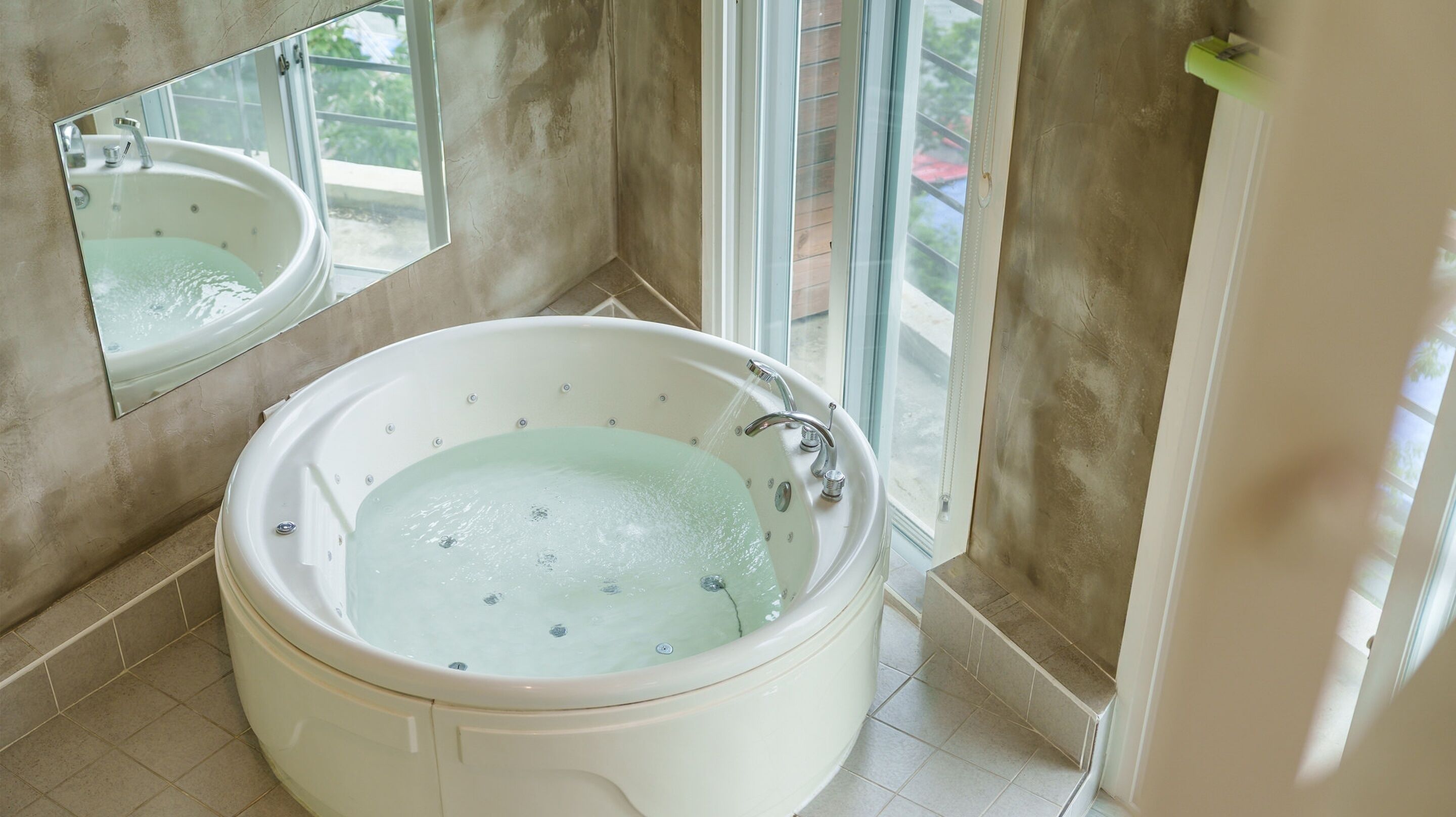 Un baño con una bañera grande, un espejo y una ventana.