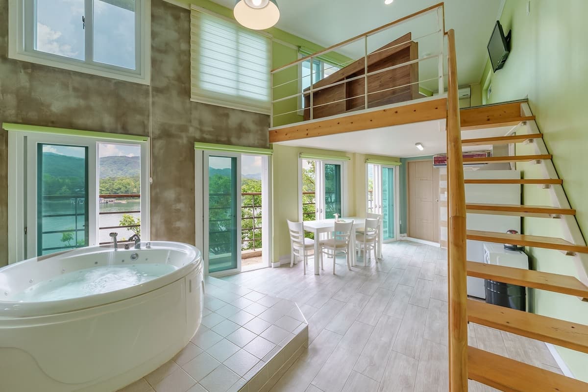 A spacious room with a large bathtub, a dining area, and a loft with a wooden staircase.