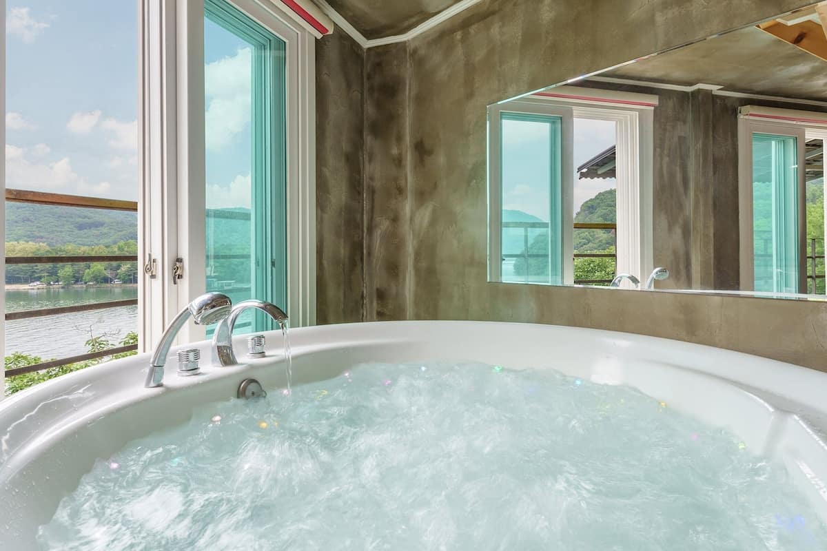A bathroom with a large bathtub, a mirror, and a view of a lake through a window.
