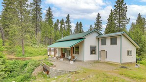 A two-story house with a green roof, a covered patio, and a stone retaining wall. - Rustic & Modern Home w/ Forest Views in Newport! (Newport)