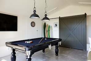 Ein Billardtisch mit Kugeln, eine Dartscheibe und Surfbretter an einer weißen Wand.