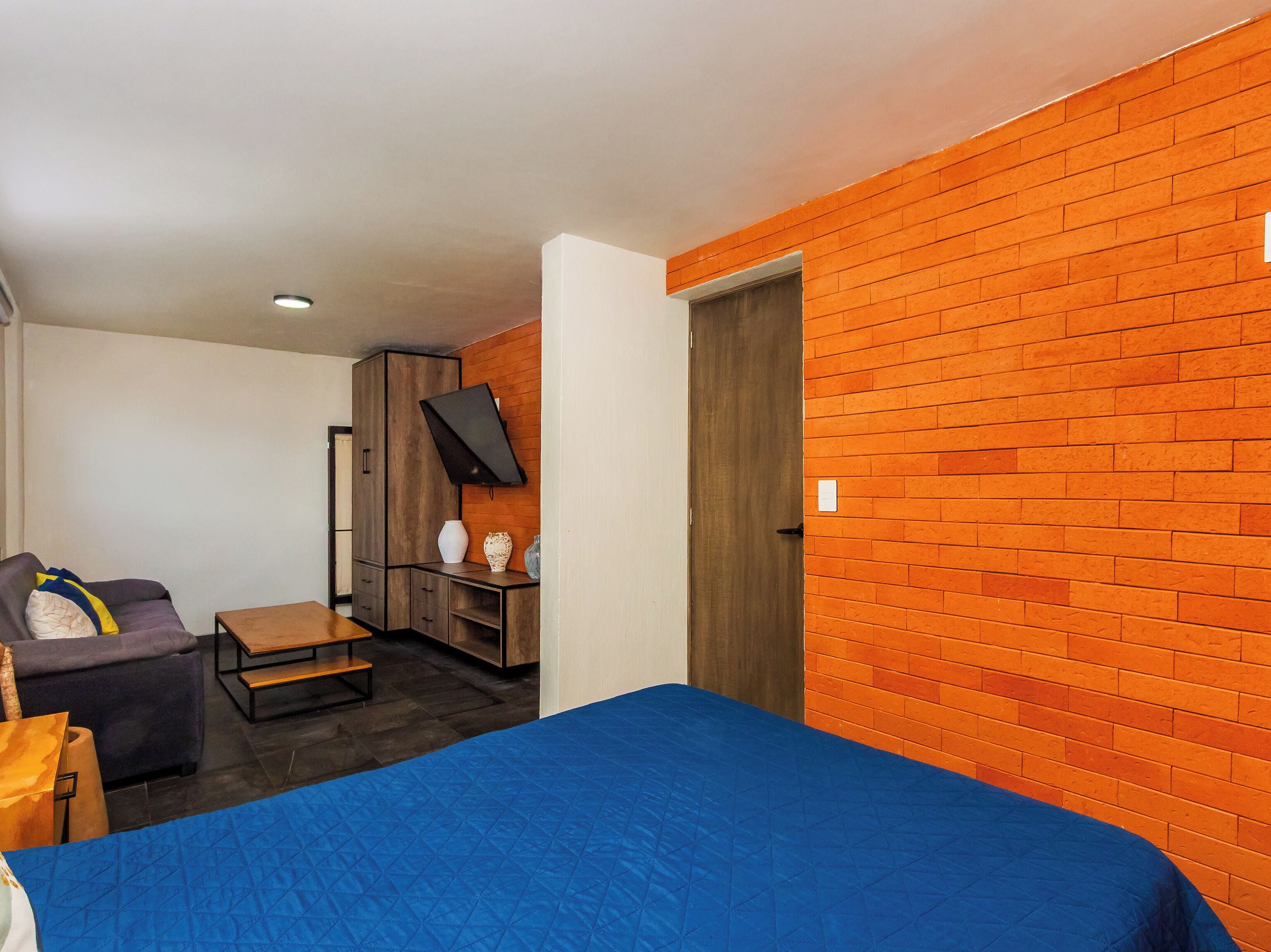 A room with a bed, a sofa, a small table, and a TV mounted on the wall.