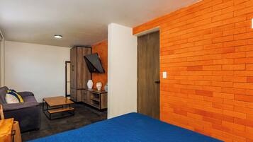 A room with a bed, a sofa, a small table, and a TV mounted on the wall.