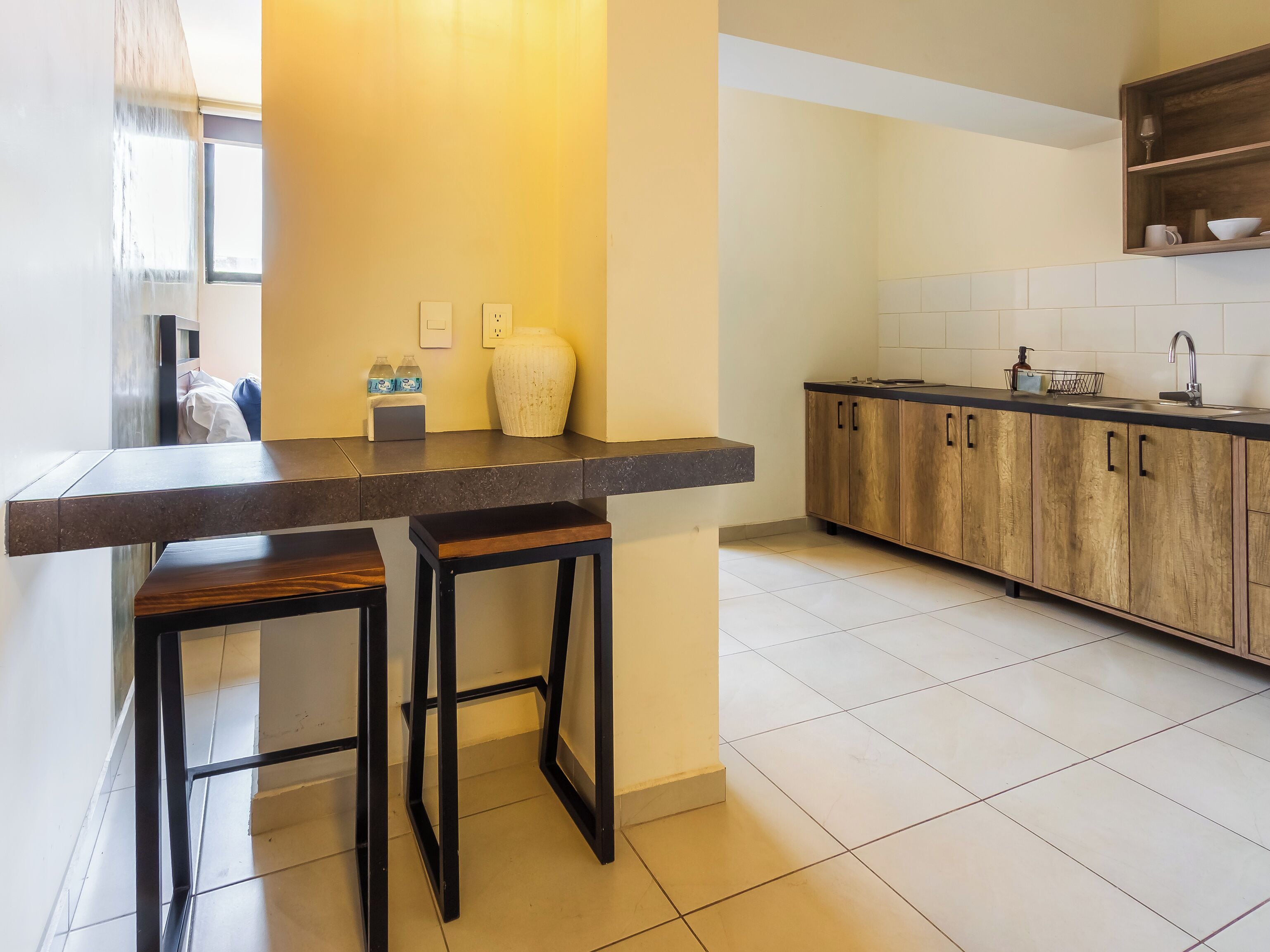 A modern kitchen with a dark countertop, wooden cabinets, and two stools.