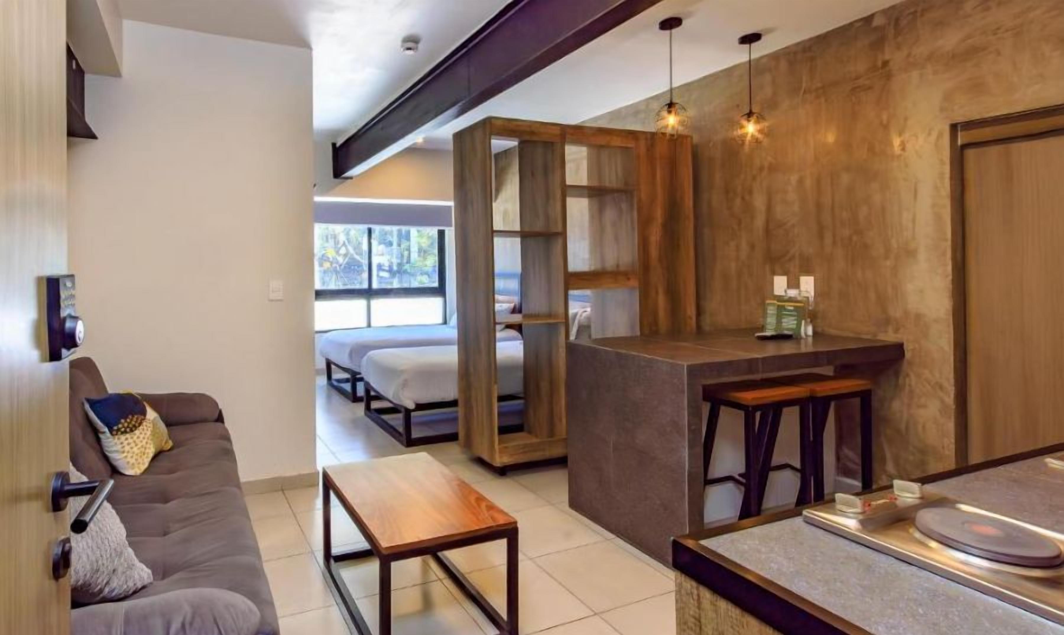 Un interior moderno con sofá, una mesa de madera, una zona de bar y vistas por una puerta abierta.
