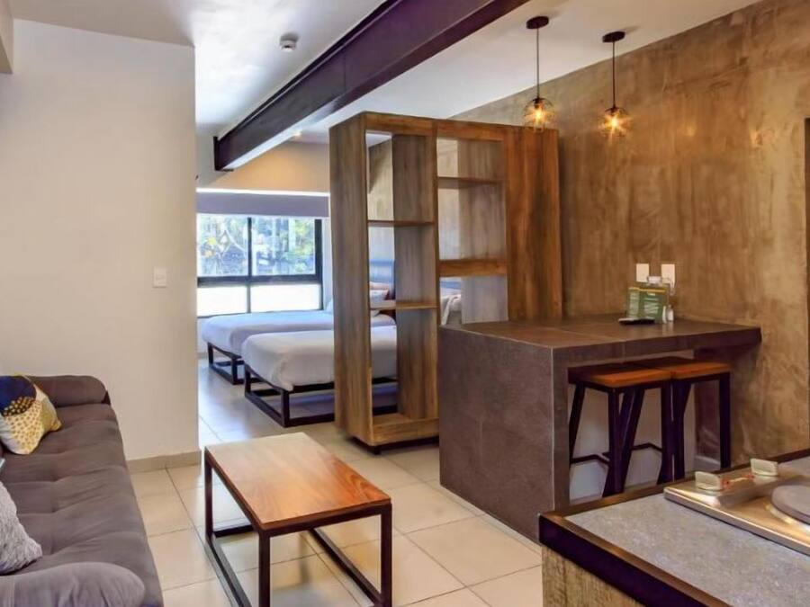 Un interior moderno con sofá, una mesa de madera, una zona de bar y vistas por una puerta abierta.