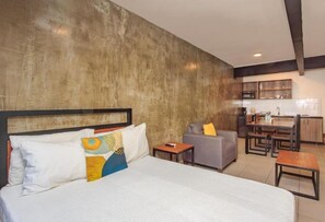 A hotel room with a large bed, a sofa, a small table, and a kitchenette in the background. - Rau Departamentos (Guadalajara)