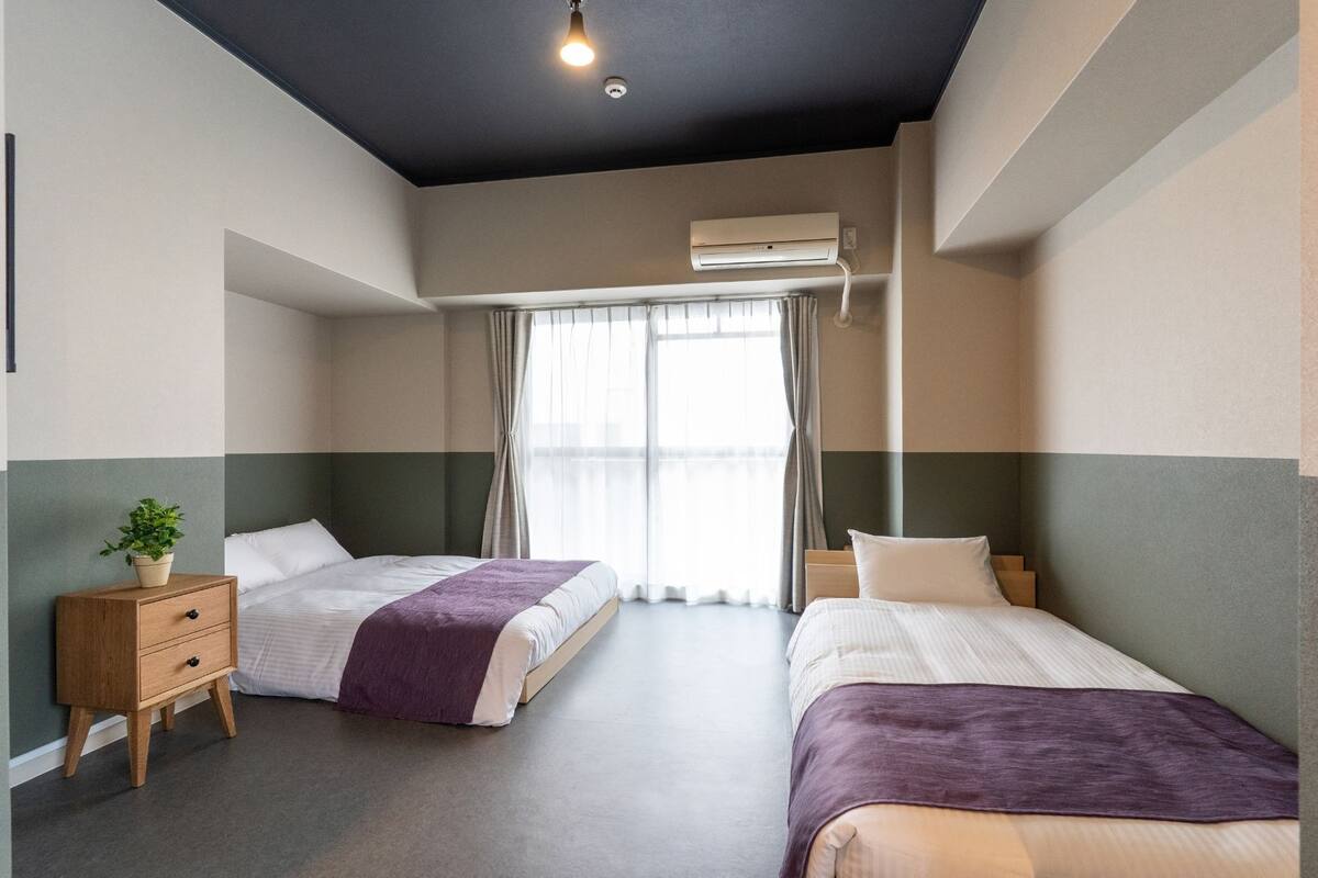 Hotellihuone, jossa on kaksi sänkyä, yöpöytä, ruukkukasvi ja ilmastointilaite.