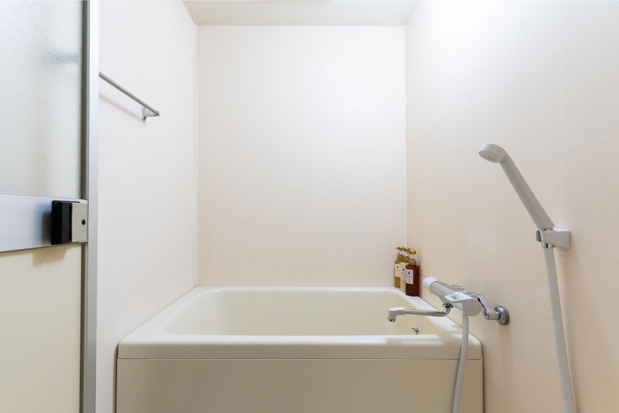 A small, white bathroom with a bathtub, a showerhead, and a towel rack.