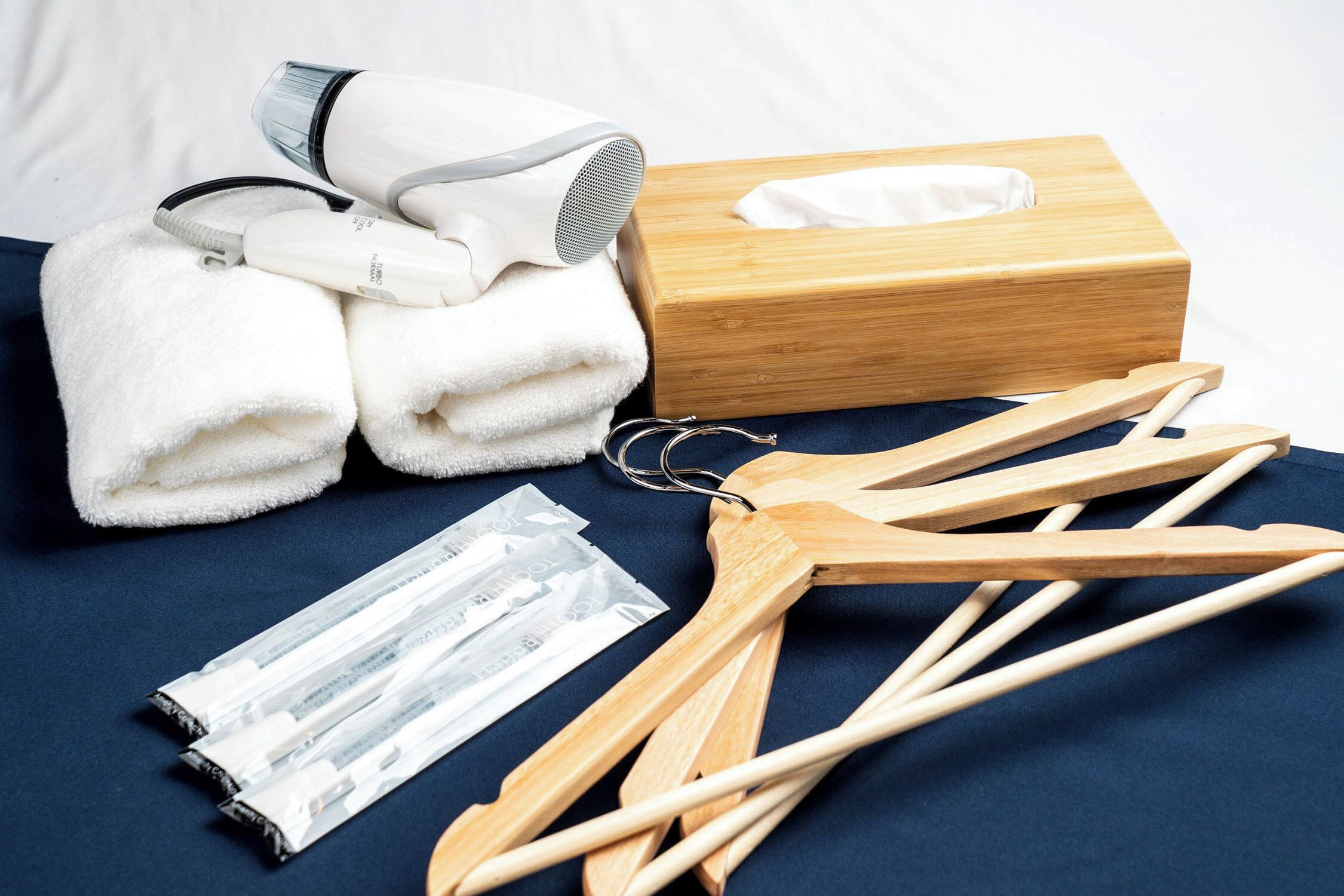 A neatly arranged set of towels, a hairdryer, a wooden hanger, and a tissue box on a dark blue surface.