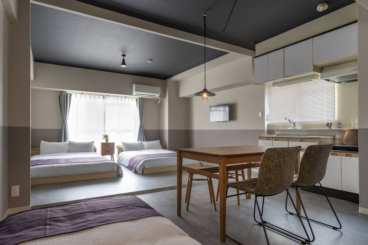 Moderni ja kompakti hotellihuone, jossa on kaksi sänkyä, ruokailutila ja pieni keittiö.