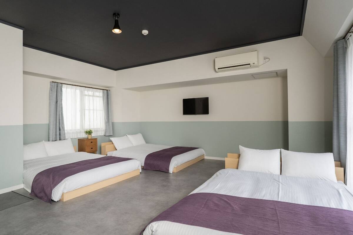 Moderni hotellihuone, jossa on kaksi sänkyä, taulutelevisio, ilmastointilaite ja ikkuna, jossa on verhot.