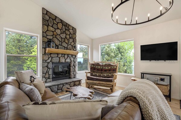 A living room with a stone fireplace, a sofa, a chair, and a television mounted on the wall.