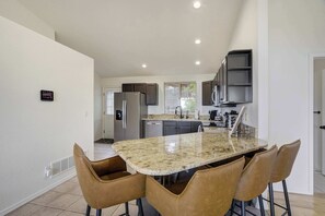 A modern kitchen with a granite countertop, stainless steel appliances, and a bar seating area.