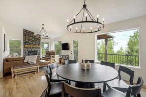 A spacious living area with a stone fireplace, a round dining table, and a large window with a view. - Cedarstone Lodge! Luxe Mountain Retreat w/ Hot Tub (Woodland Park)