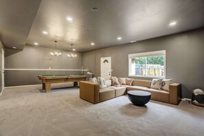 Une pièce avec une table de billard, un canapé, une table basse et une fenêtre donnant sur un beau paysage.