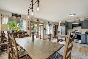 Une table à manger en bois, avec des chaises, un vase orné de branches et une enseigne au-dessus de la fenêtre.