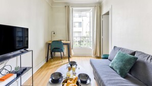 Ein modernes Wohnzimmer mit Fernseher, Esstisch mit Frühstücksangebot, einer Couch und Blick auf den Balkon.