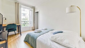Ein Schlafzimmer mit Bett, Schreibtisch, Stuhl, Lampe und Blick ins Freie.