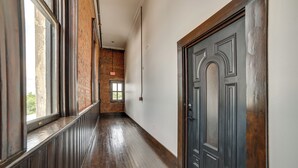 Un corridoio con pavimento in legno, parete in mattoni e porta in legno scuro.