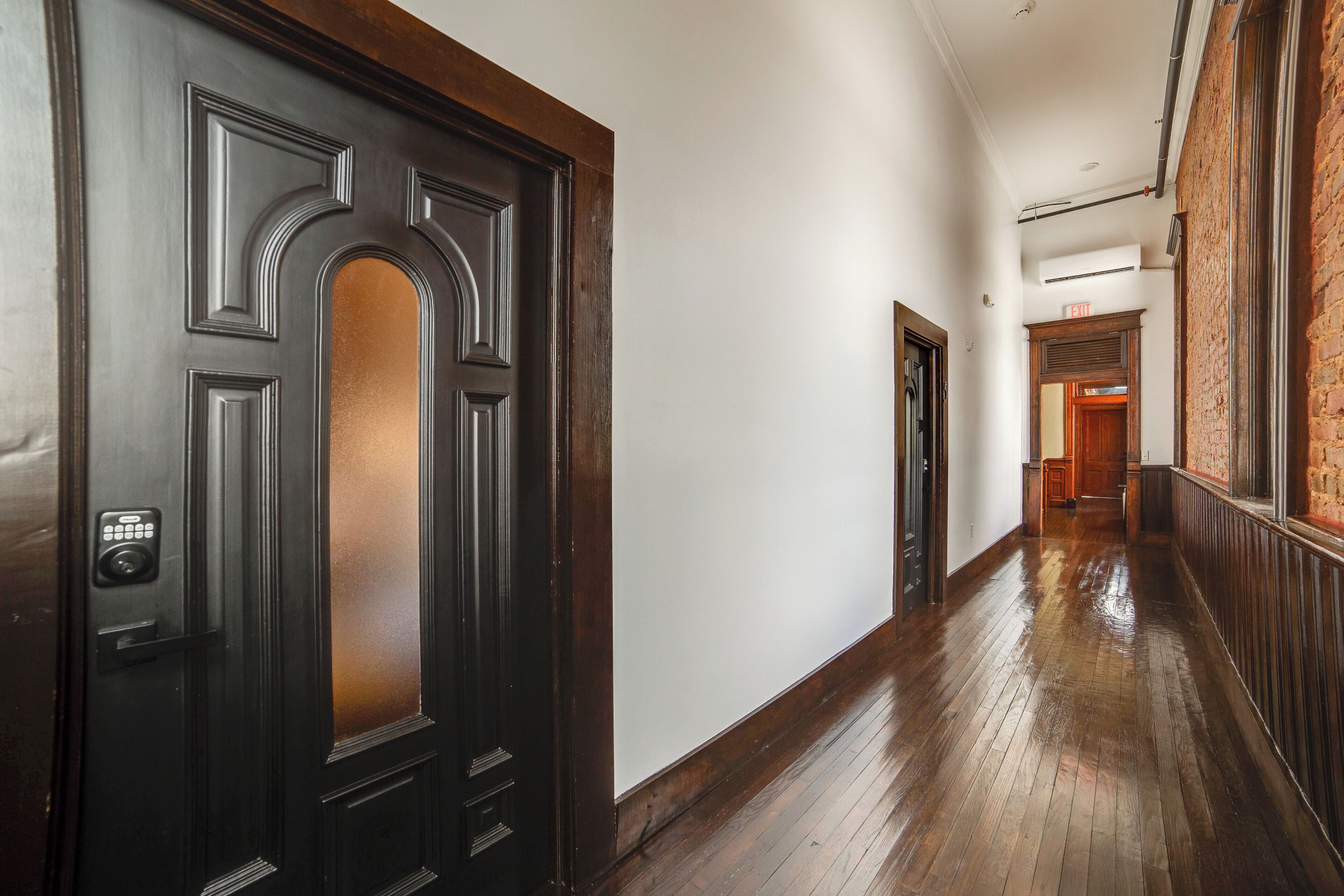A hallway with a dark wooden door, white walls, and a wooden floor.