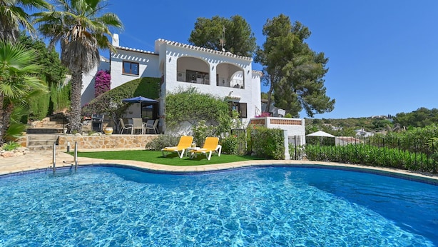 A pool with two yellow lounge chairs, a white building with arches, and a clear blue sky. - Ines Isabel - Javea, Costa Blanca (Javea)
