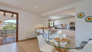 A modern kitchen with white cabinets, stainless steel appliances, and a glass dining table with white chairs. - Ines Isabel - Javea, Costa Blanca (Javea)