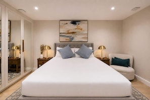 A bedroom with a large bed, bedside lamps, a chair, and a painting on the wall. - Chelsea 4‑BR, 4 Ensuites | Roof Deck, Quiet Street (London)
