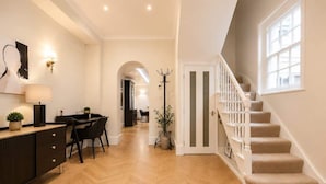 Un couloir avec un escalier, un bureau avec une lampe et un porte-manteau.
