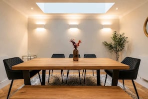 A modern dining room with a wooden table, black chairs, a vase with flowers, and a skylight. - Chelsea 4‑BR, 4 Ensuites | Roof Deck, Quiet Street (London)