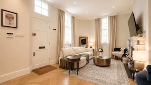 Un salon avec un canapé, une table basse et un téléviseur. Il y a une porte, des fenêtres et un tapis.