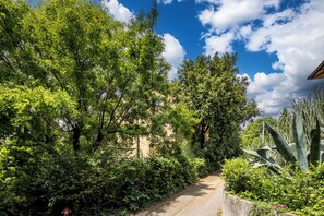 A narrow pathway flanked by dense greenery and a building with a sloped roof. - Nurli Apt Near Glavanovo Beach (Rijeka)