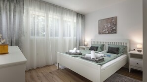 A neatly arranged bedroom with a bed, bedside tables, a desk, and a window with sheer curtains. - Nurli Apt Near Glavanovo Beach (Rijeka)
